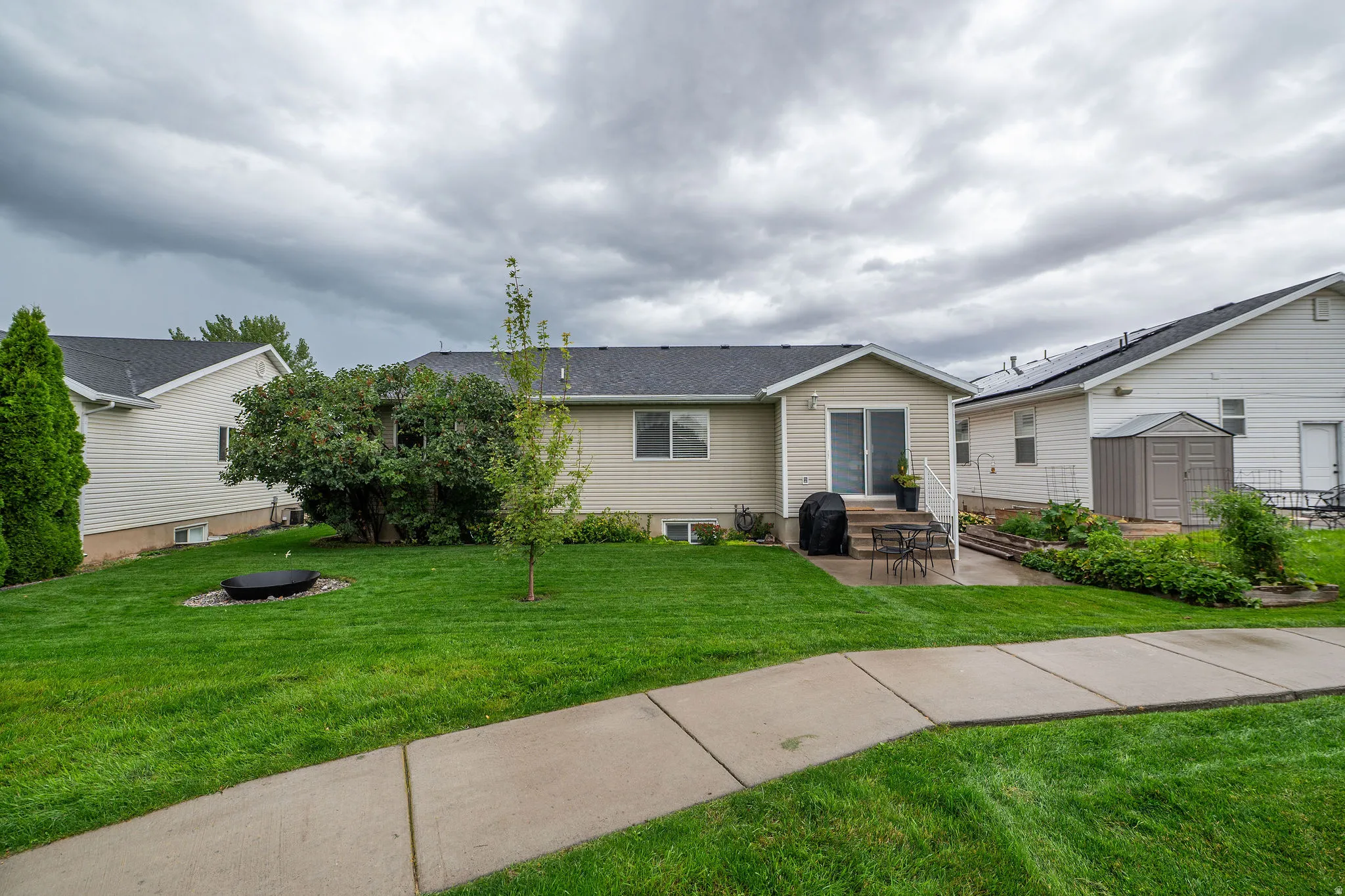 Expansive green lawn, concrete patio, sliding glass door, mature landscaping, and a concrete walkway
