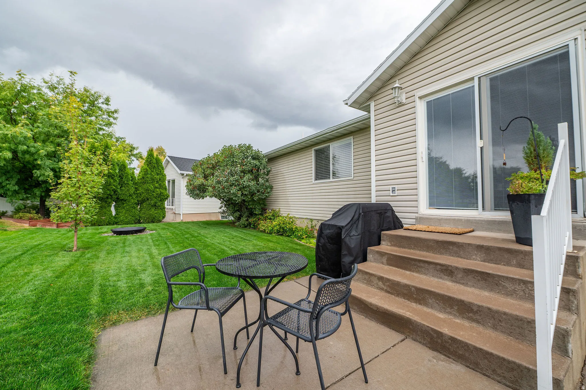 Manicured lawn, mature trees, concrete patio, concrete steps, sliding glass door