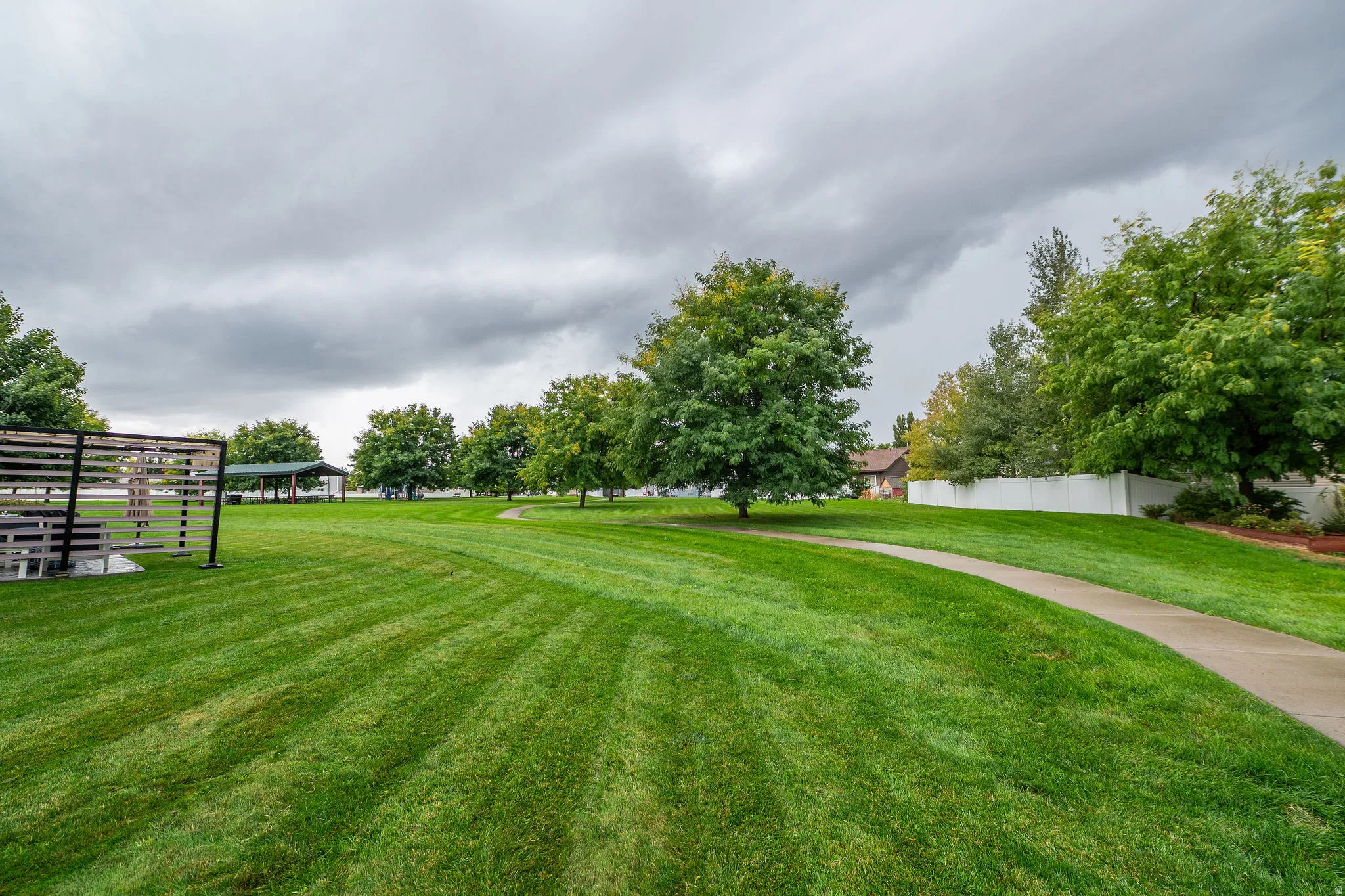 Expansive green space featuring a paved pathway, mature trees, and a slatted privacy screen structure