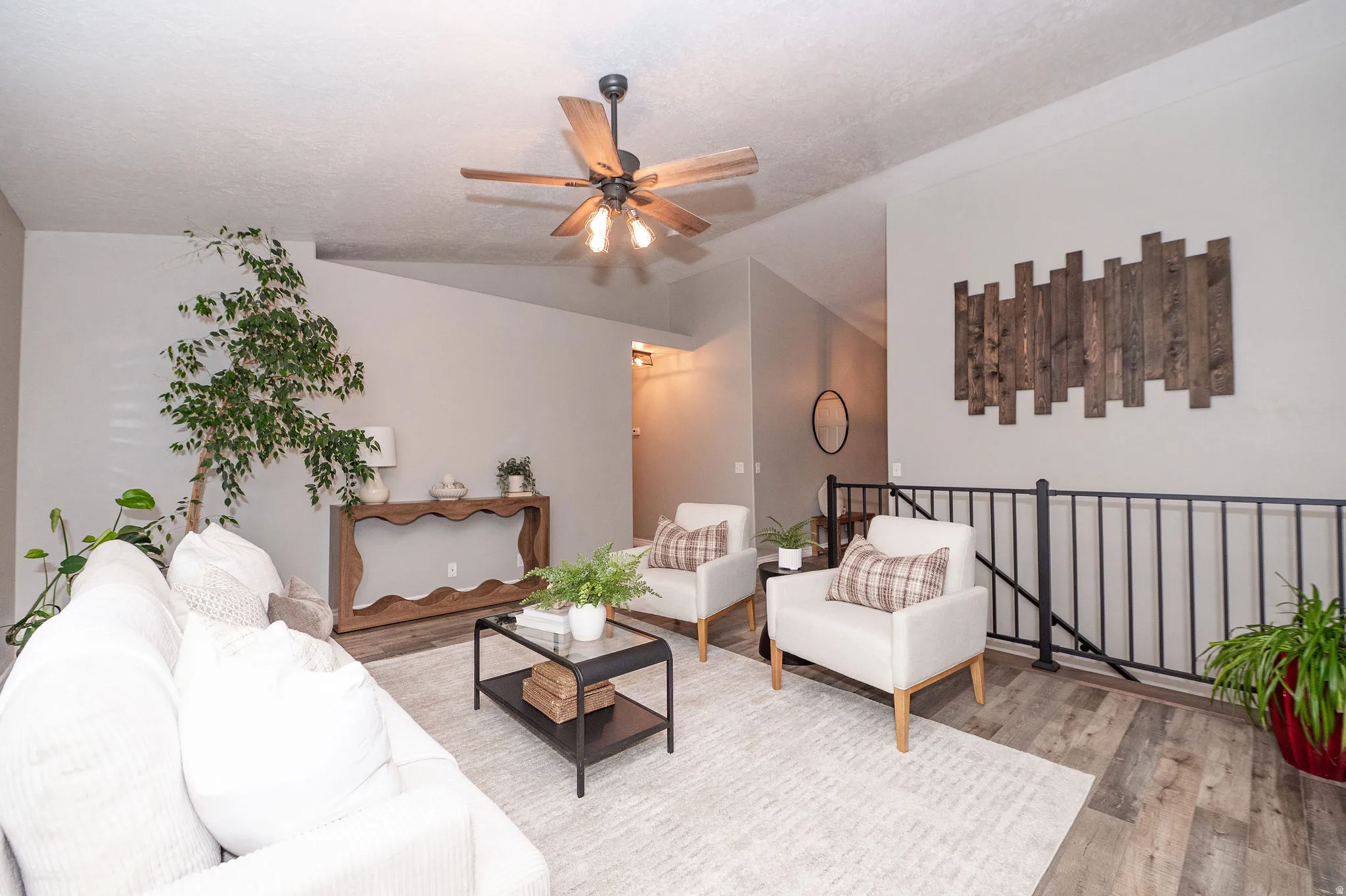 Wood-finish flooring, a ceiling fan with integrated lighting, and a console table with a decorative base