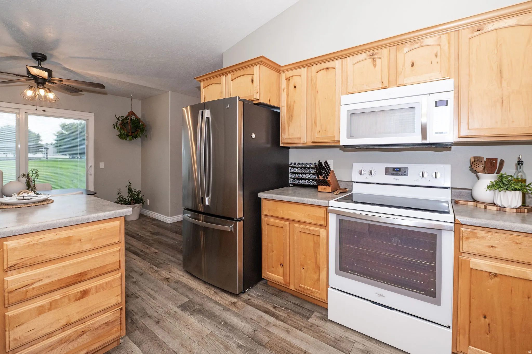 Wood-finish flooring with light wood cabinetry, stone-finish countertops, and stainless-steel appliances
