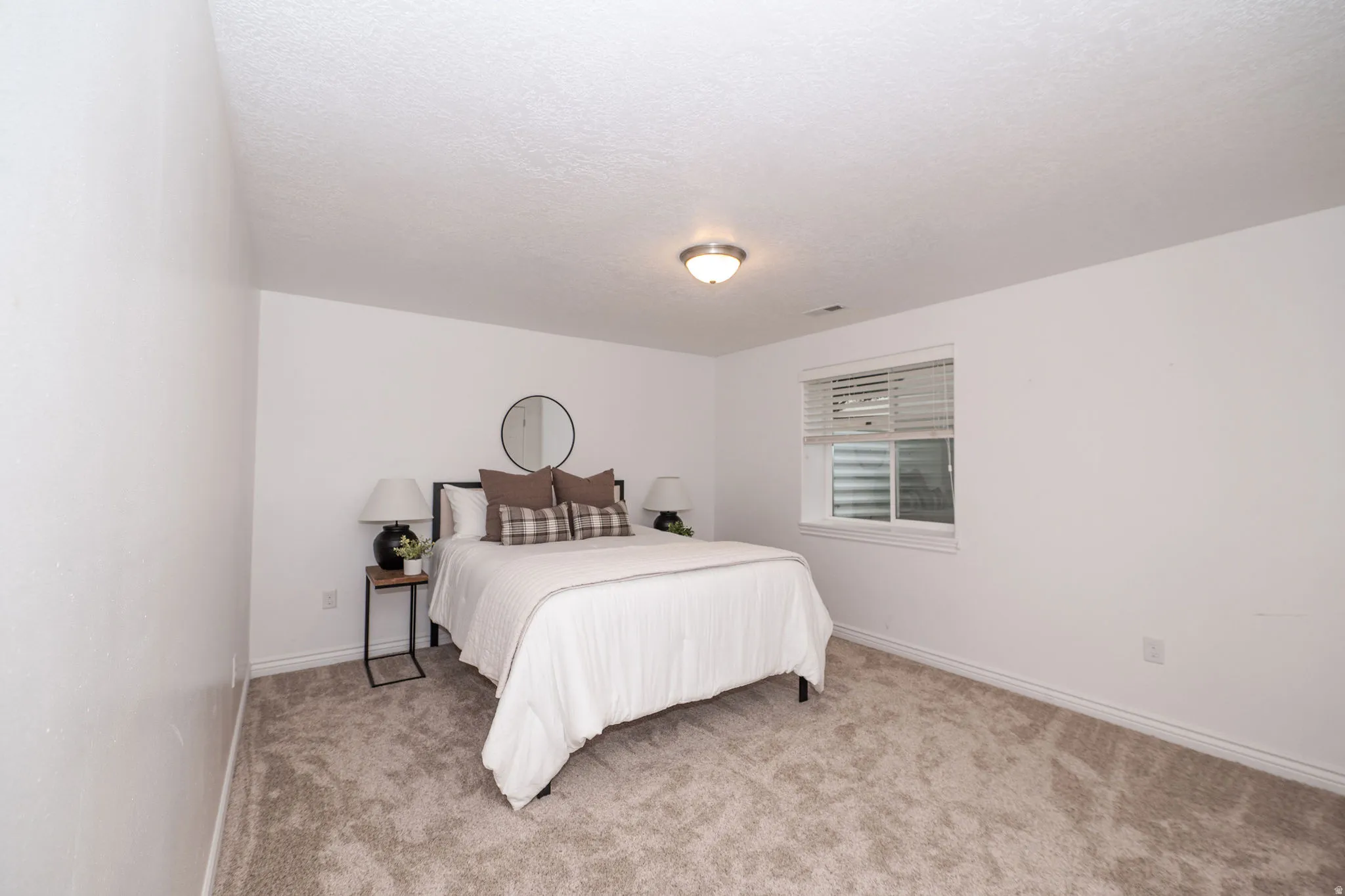 Wall-to-wall carpeting with light-toned walls and trim, featuring a flush-mount ceiling light and a window with blinds