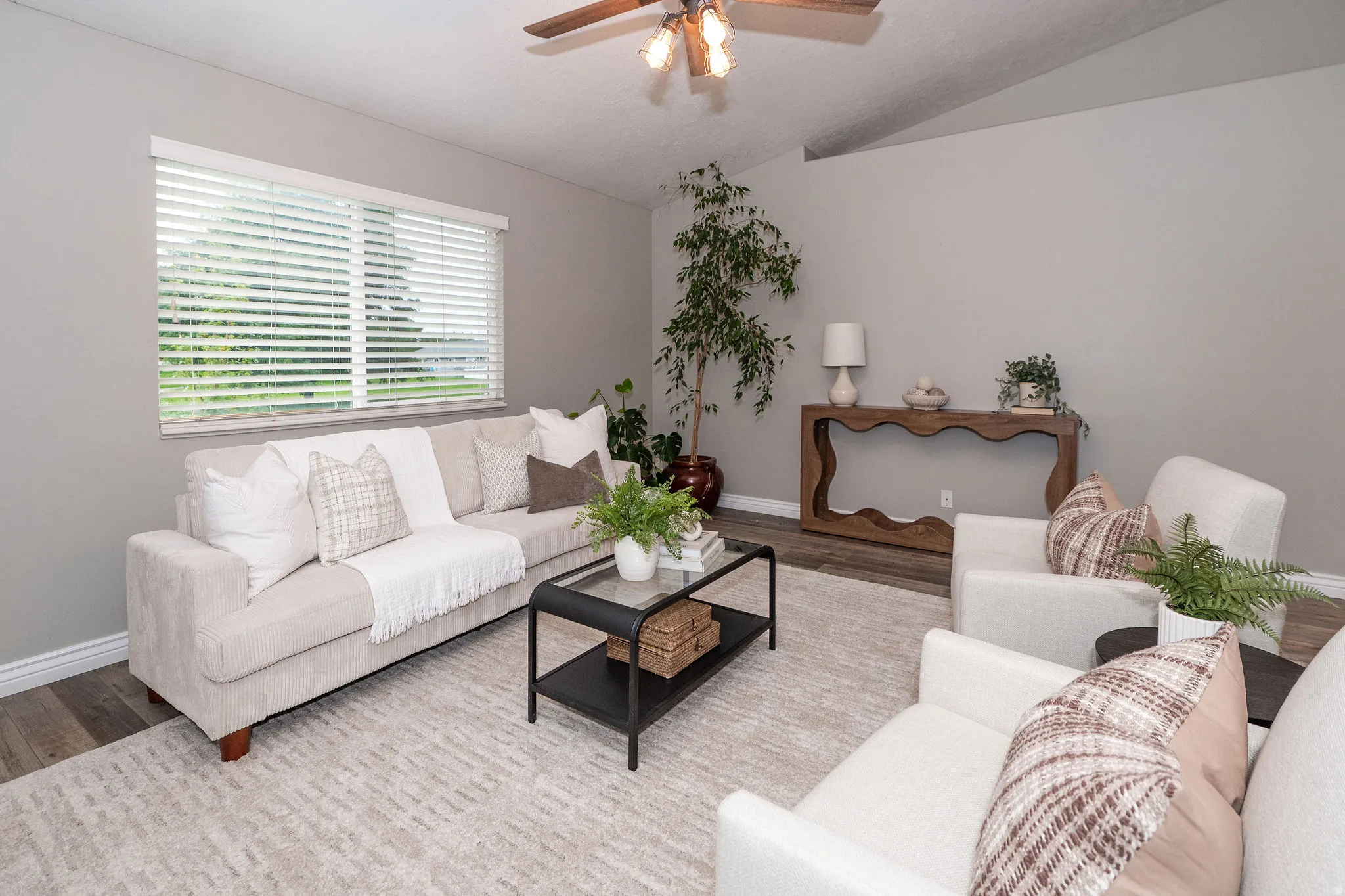 Vaulted ceilings with a ceiling fan light fixture, wood-finish flooring, a large window with blinds, and painted walls