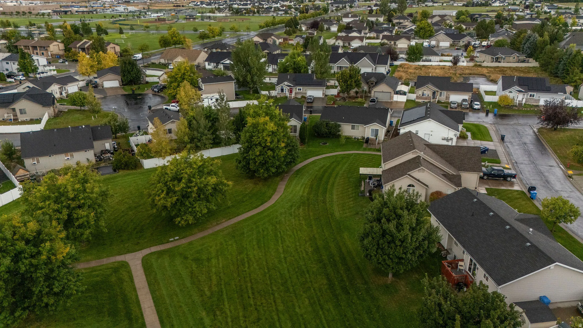 Expansive green space with mature trees and a paved walking path, surrounded by a residential neighborhood