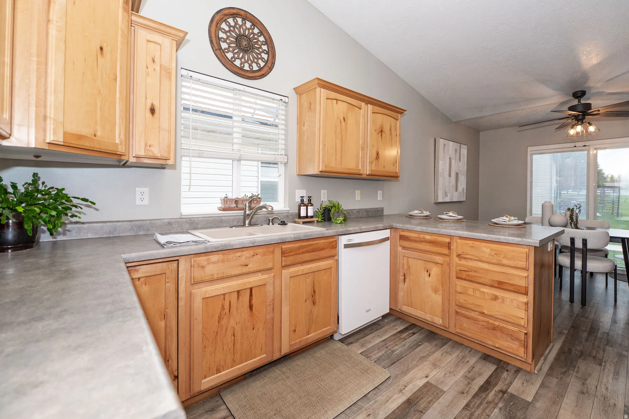 Open-concept kitchen featuring wood-finish cabinetry, a stainless steel sink, a white built-in dishwasher, and wood-finish flooring