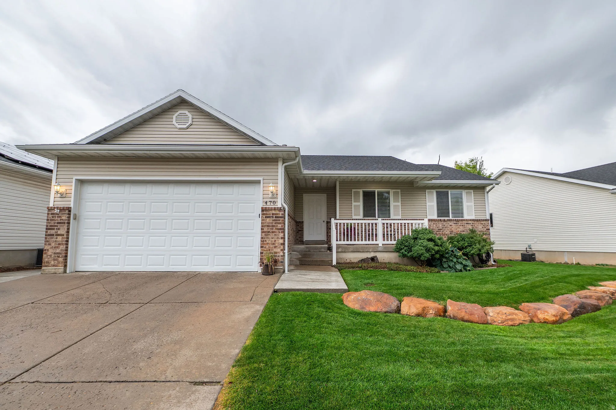Exterior showcasing a two-car garage, front porch with white railing, brick accents, and a landscaped front yard with decorative boulders