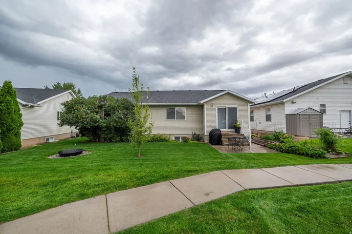 Expansive green lawn, concrete patio, sliding glass door, mature landscaping, and a concrete walkway