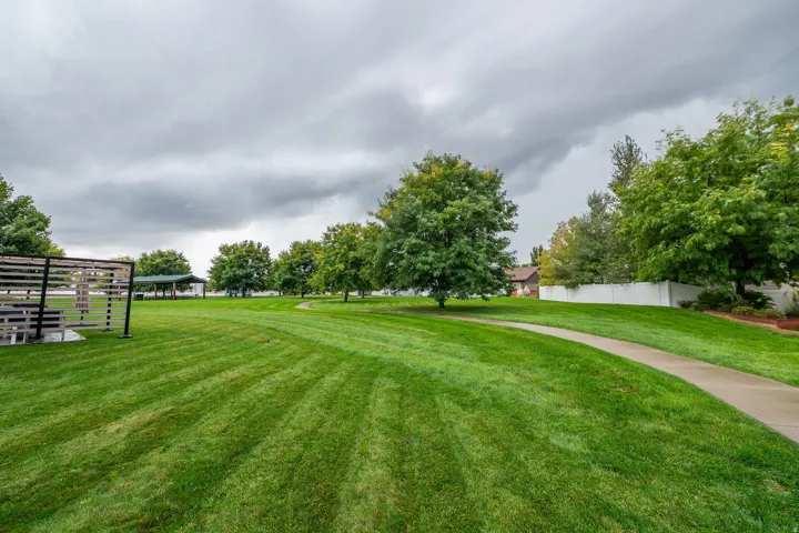 Expansive green space featuring a paved pathway, mature trees, and a slatted privacy screen structure