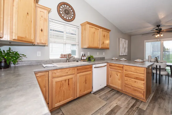Open-concept kitchen featuring wood-finish cabinetry, a stainless steel sink, a white built-in dishwasher, and wood-finish flooring