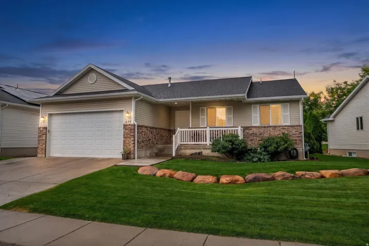 Single-story exterior with a two-car garage, brick and siding facade, covered front porch with railing, and a landscaped front yard with decorative stones