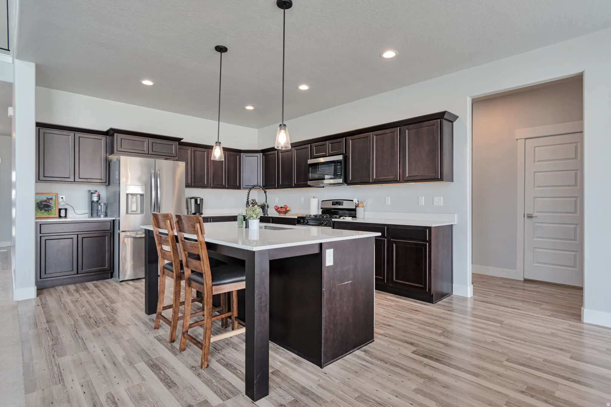 Kitchen featuring dark wood cabinetry, light countertops, wood-finish flooring, stainless steel appliances, and an island with pendant lighting