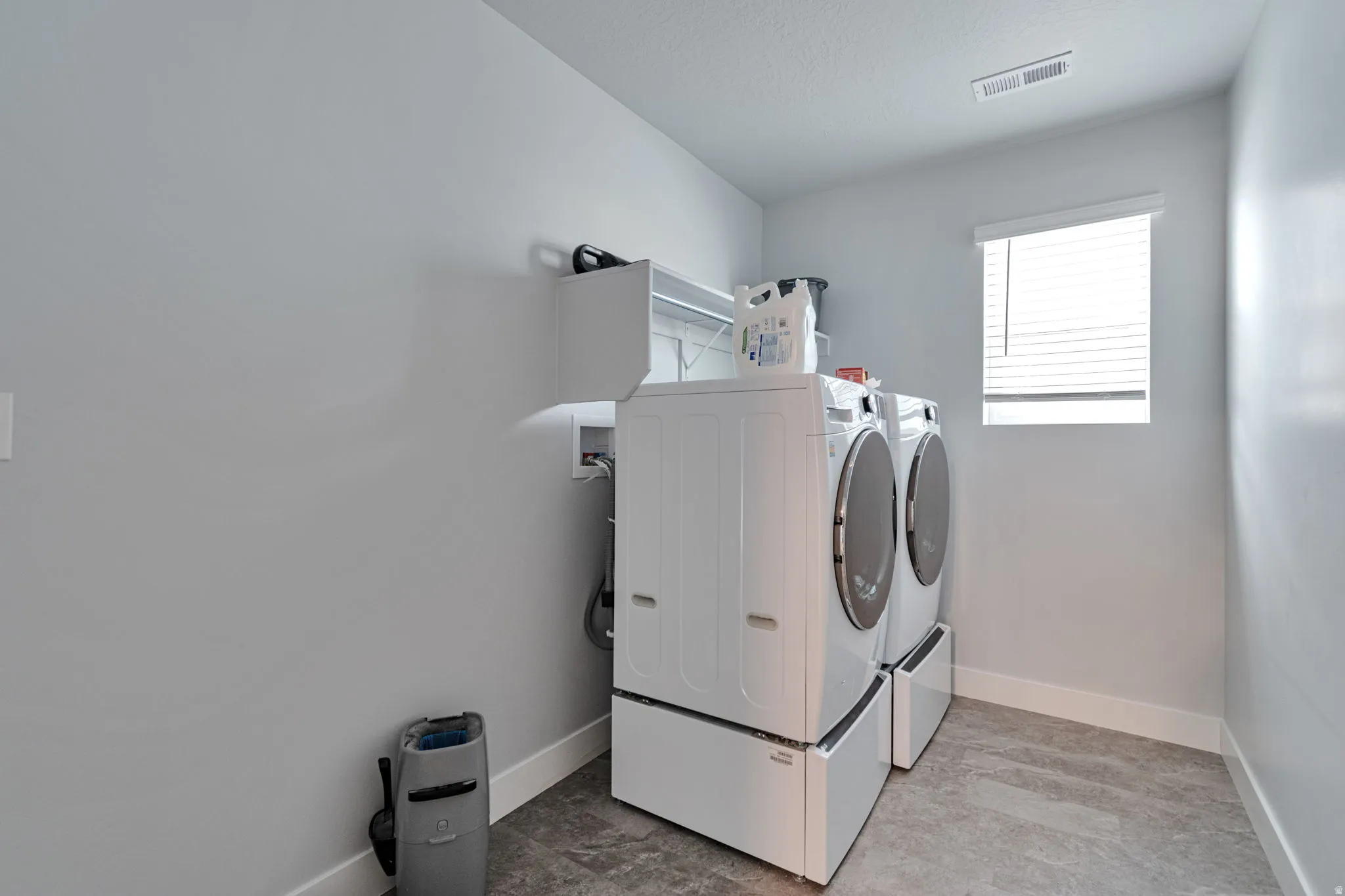 Laundry area featuring a window with blinds, overhead shelving, and gray-toned flooring