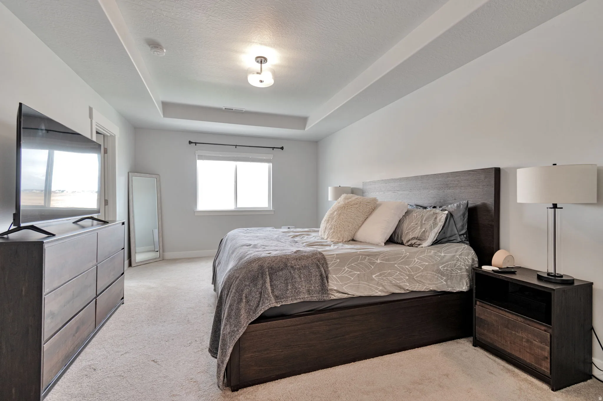 Recessed ceiling with central light fixture, wall-to-wall carpeting, and window with dark rod