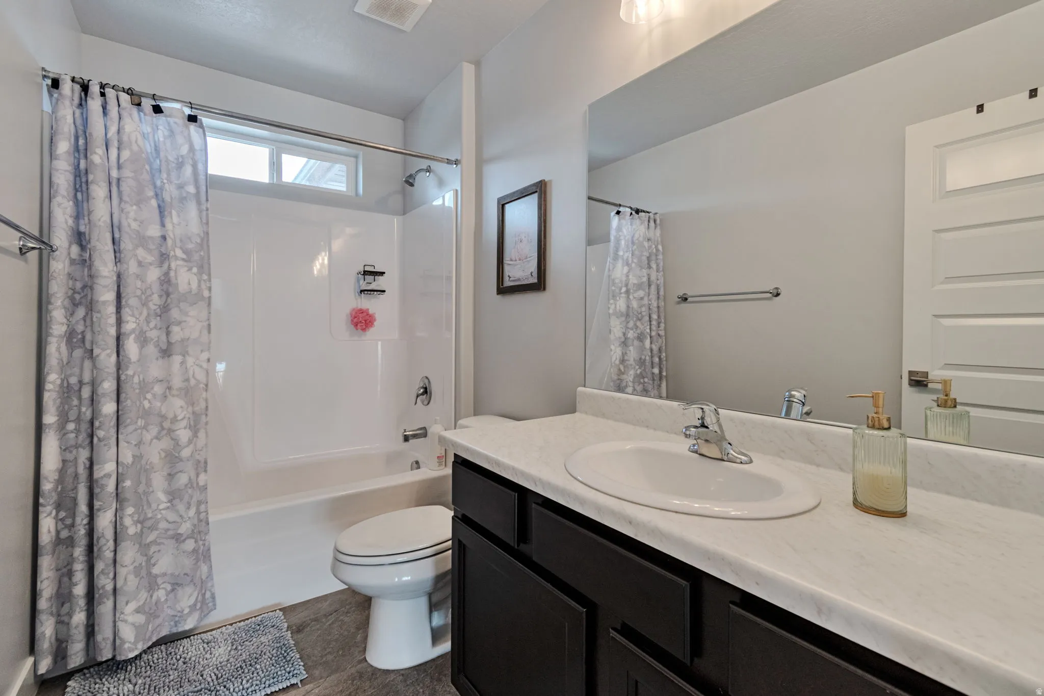 Bathroom featuring a single vanity with dark wood-finish cabinetry, a large integrated mirror, a white bathtub with an overhead shower, and a high transom window