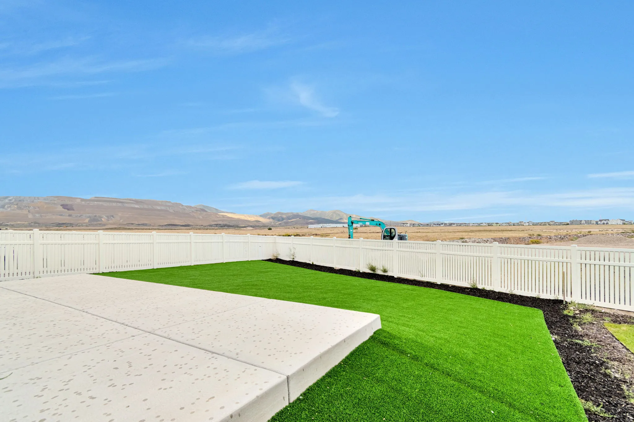 Expansive concrete patio with a manicured lawn area and white privacy fencing