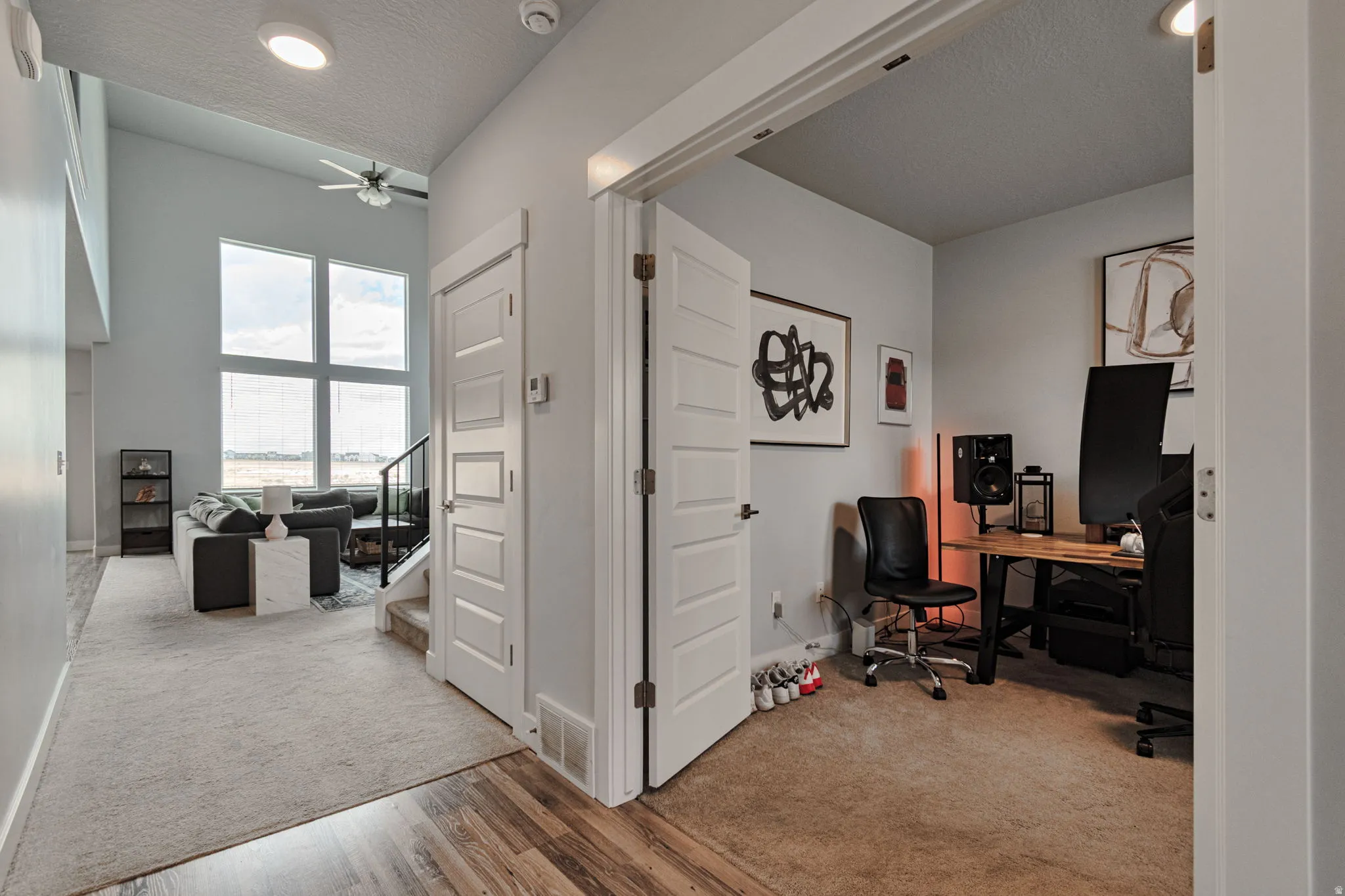 Two-story ceiling, large windows, ceiling fan, wood-finish flooring, and white paneled doors