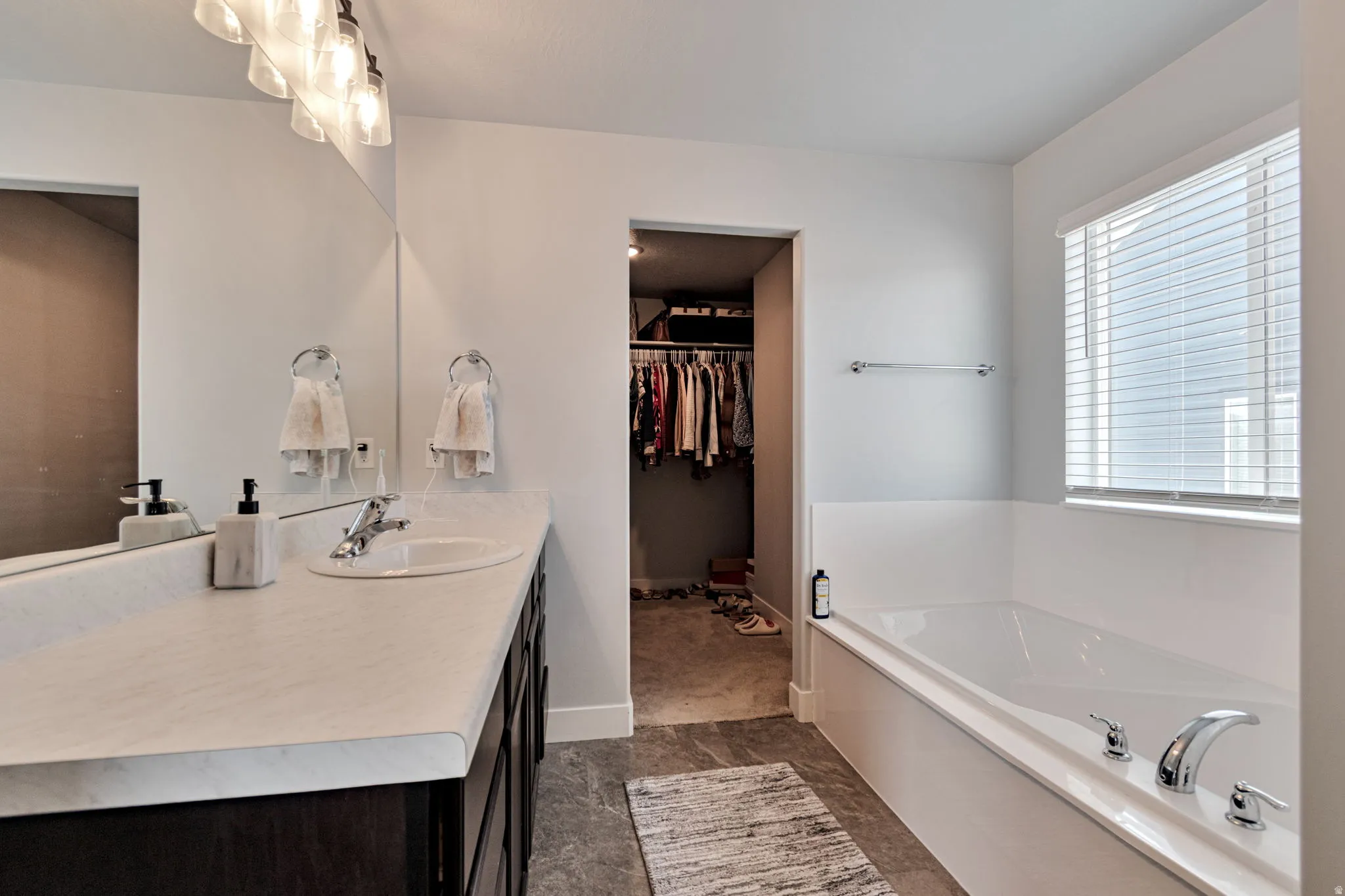 Spacious bathroom with a built-in soaking tub, vanity with an integrated sink, broad mirror, and a window with horizontal blinds