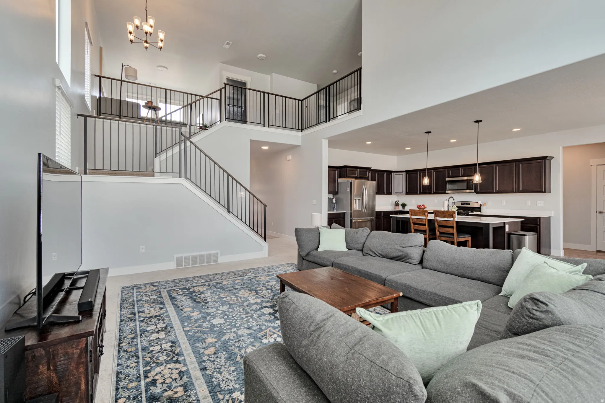 Open-concept living area featuring a two-story ceiling, kitchen with dark wood-finish cabinetry, and a staircase with metal railings