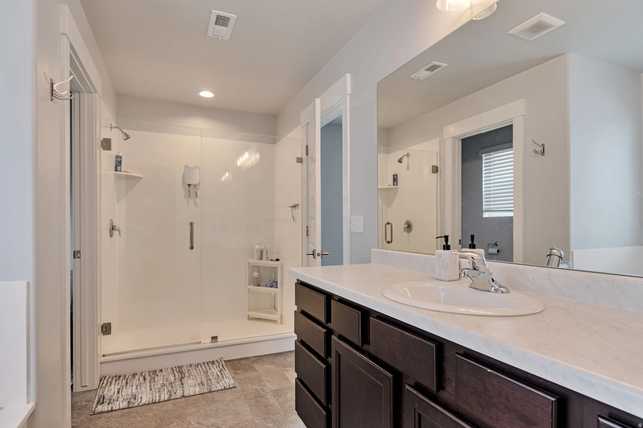 Walk-in shower with clear glass enclosure, single vanity with dark wood-finish cabinetry, integrated sink, and large wall-mounted mirror