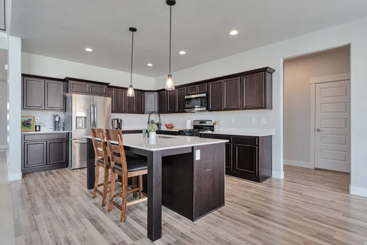 Kitchen featuring dark wood cabinetry, light countertops, wood-finish flooring, stainless steel appliances, and an island with pendant lighting
