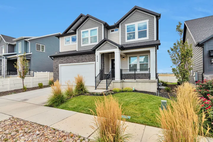 Two-story residence featuring a multi-tone facade with stone and siding elements, an attached two-car garage, a covered front porch with black railings, and a concrete driveway