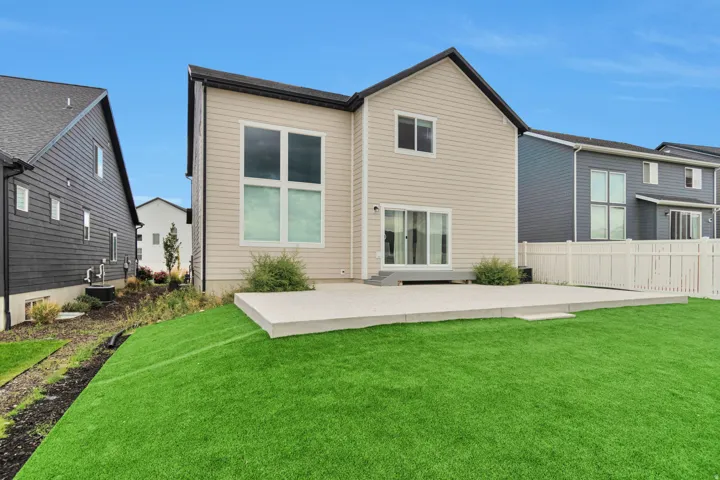 Expansive artificial turf lawn with a large concrete patio, white vinyl fencing, and sliding glass doors