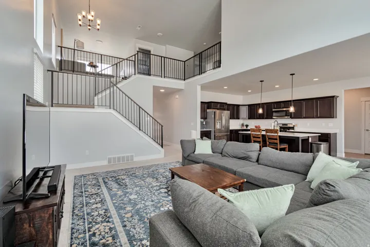 Open-concept living area featuring a two-story ceiling, kitchen with dark wood-finish cabinetry, and a staircase with metal railings