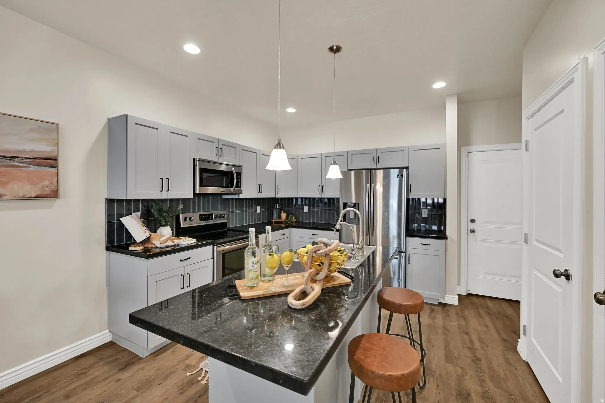 Kitchen featuring light gray cabinetry, dark countertops, dark tile backsplash, stainless steel appliances, and wood-finish flooring