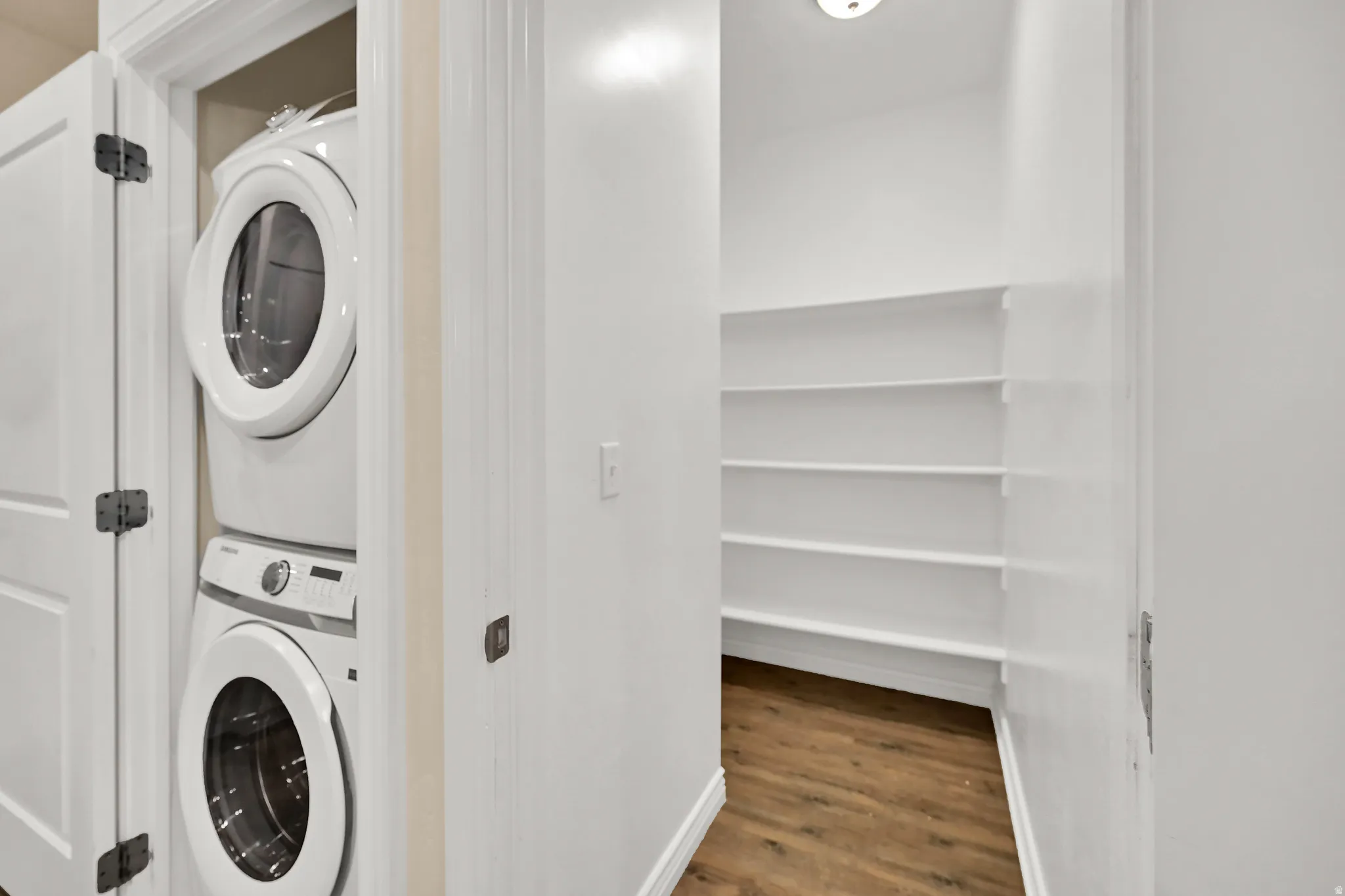Laundry closet with stacked appliances and a pantry featuring multiple shelving units and wood-finish flooring