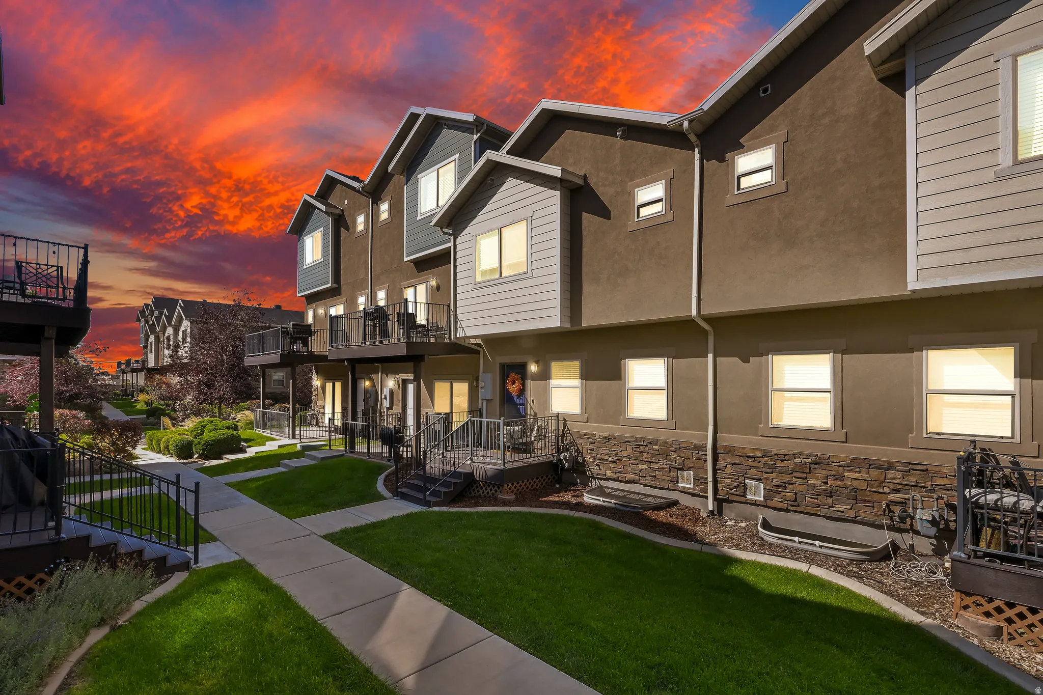 Townhome exterior with stone accent siding, private balconies, and landscaped grounds featuring manicured lawns and concrete pathways