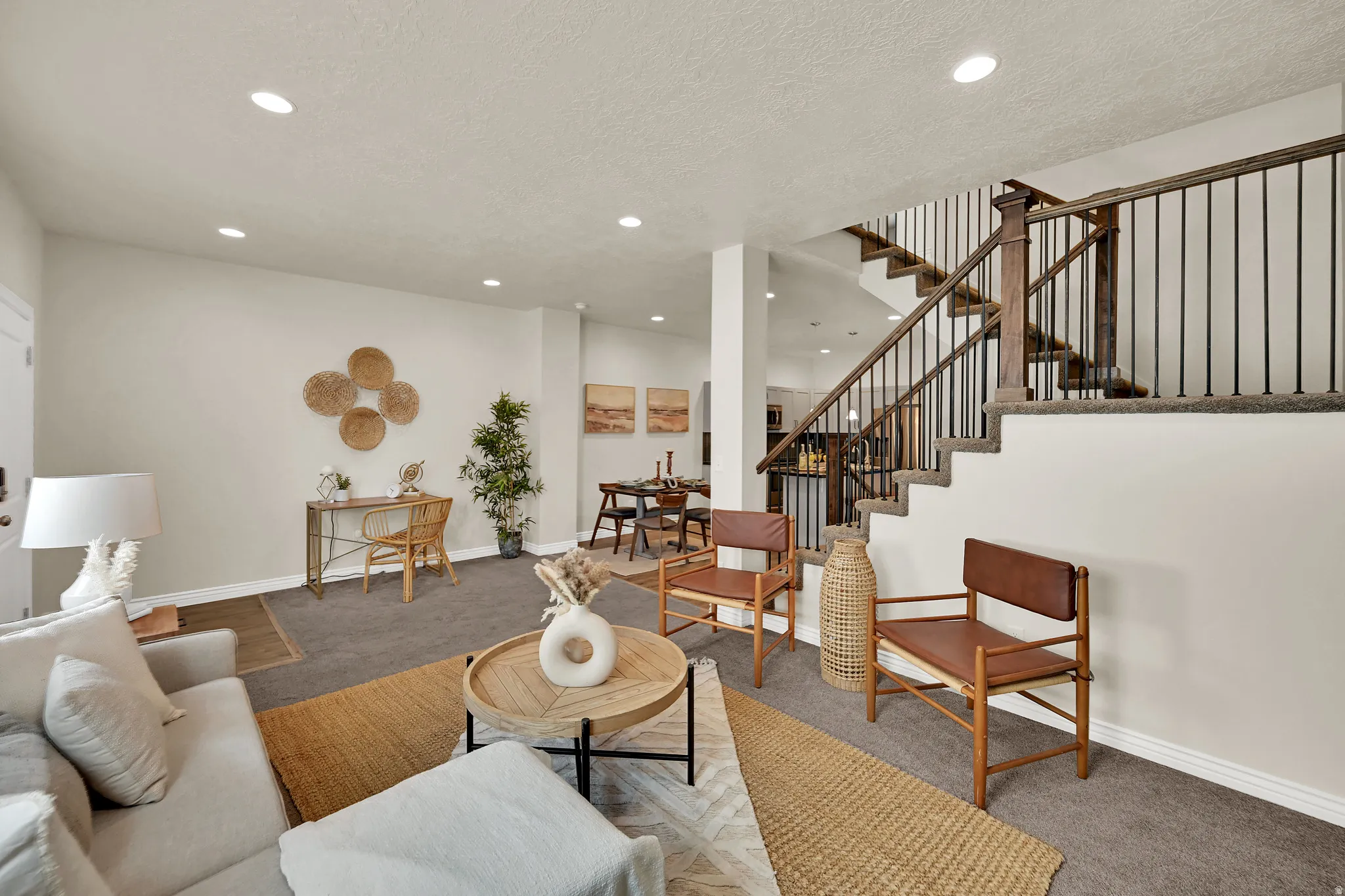 Open concept living area with recessed lighting, carpeted flooring, and a staircase featuring wood and iron railings