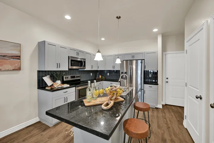 Kitchen featuring light gray cabinetry, dark countertops, dark tile backsplash, stainless steel appliances, and wood-finish flooring