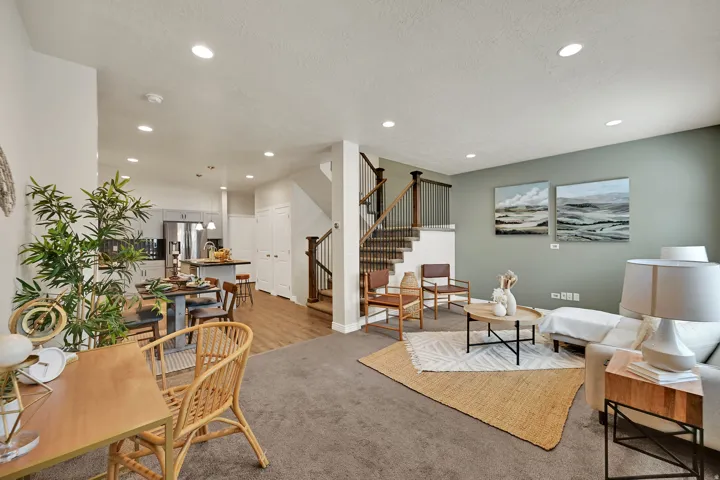 Open-concept living area with recessed lighting, carpeted flooring, and a staircase featuring dark wood newel posts and metal balusters