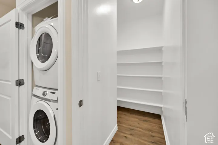 Laundry closet with stacked appliances and a pantry featuring multiple shelving units and wood-finish flooring