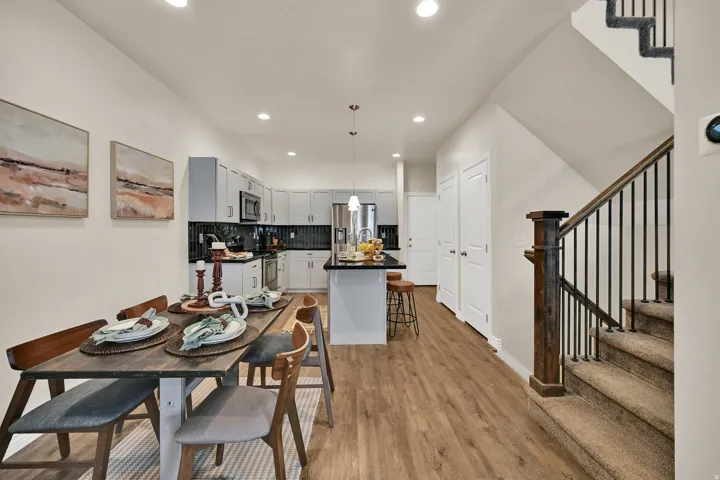 Open-concept living space featuring wood-finish flooring, a kitchen with stainless steel appliances, a center island, and a staircase with a dark wood newel post and metal balusters