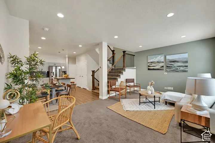 Open-concept living area with recessed lighting, carpeted flooring, and a staircase featuring dark wood newel posts and metal balusters