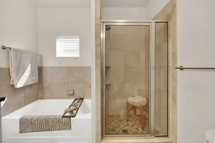 Built-in bathtub with tiled surround, adjacent to a glass-enclosed shower with tiled walls and floor