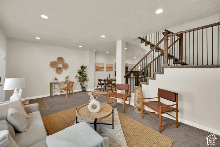 Open concept living area with recessed lighting, carpeted flooring, and a staircase featuring wood and iron railings