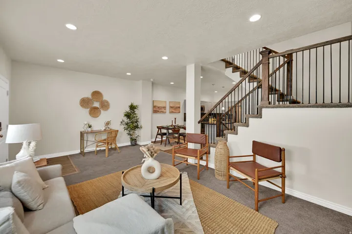 Open concept living area with recessed lighting, carpeted flooring, and a staircase featuring wood and iron railings