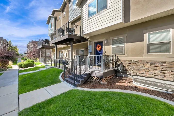 Exterior featuring stone veneer accents, multi-level balconies with black railings, and a manicured lawn with a concrete pathway
