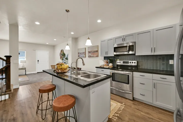 Kitchen with light gray cabinetry, stainless steel appliances, dark countertops, and wood-finish flooring