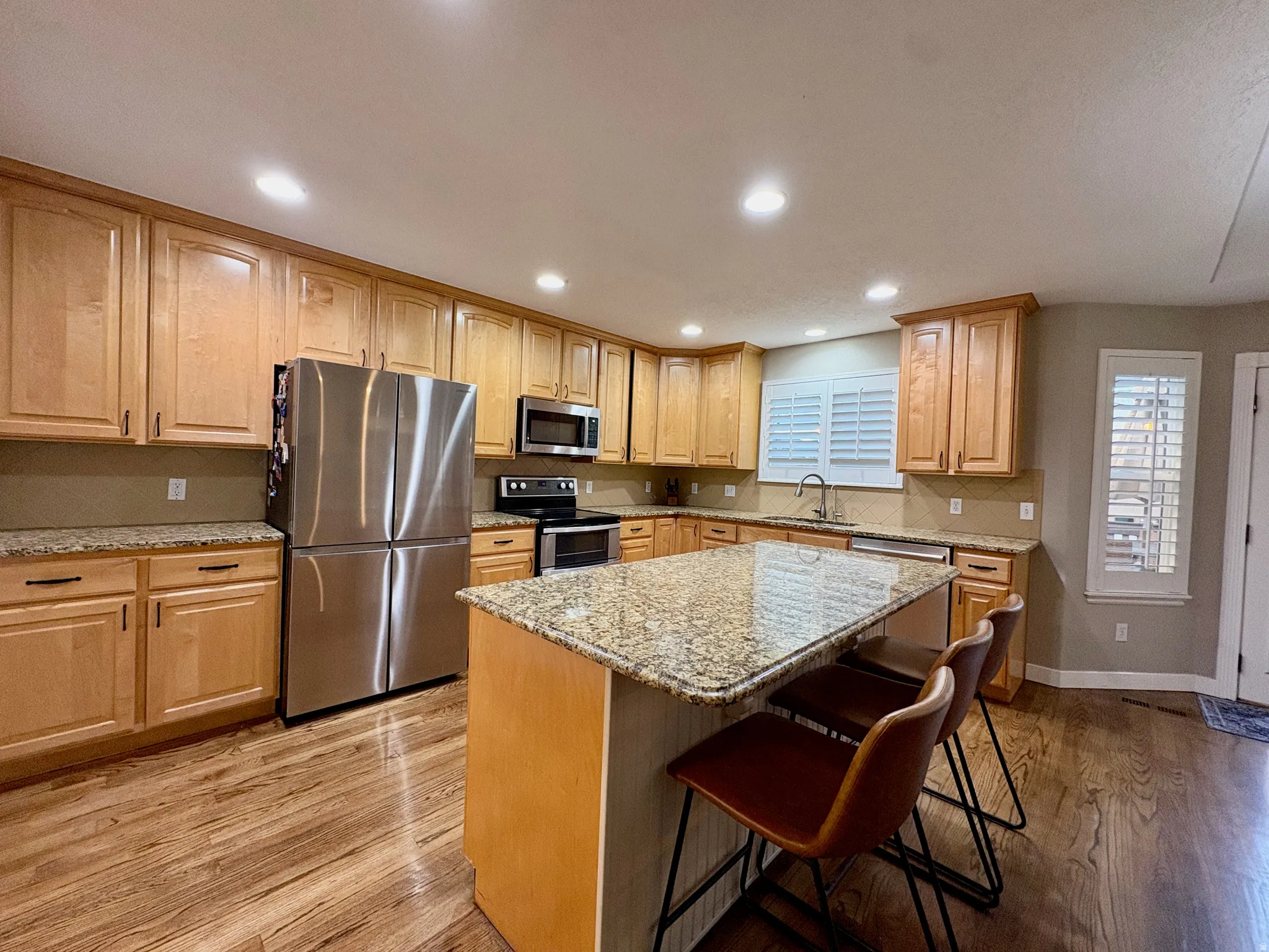 Kitchen featuring light wood cabinetry, recessed lighting, stainless steel appliances, granite countertops, and wood-finish flooring