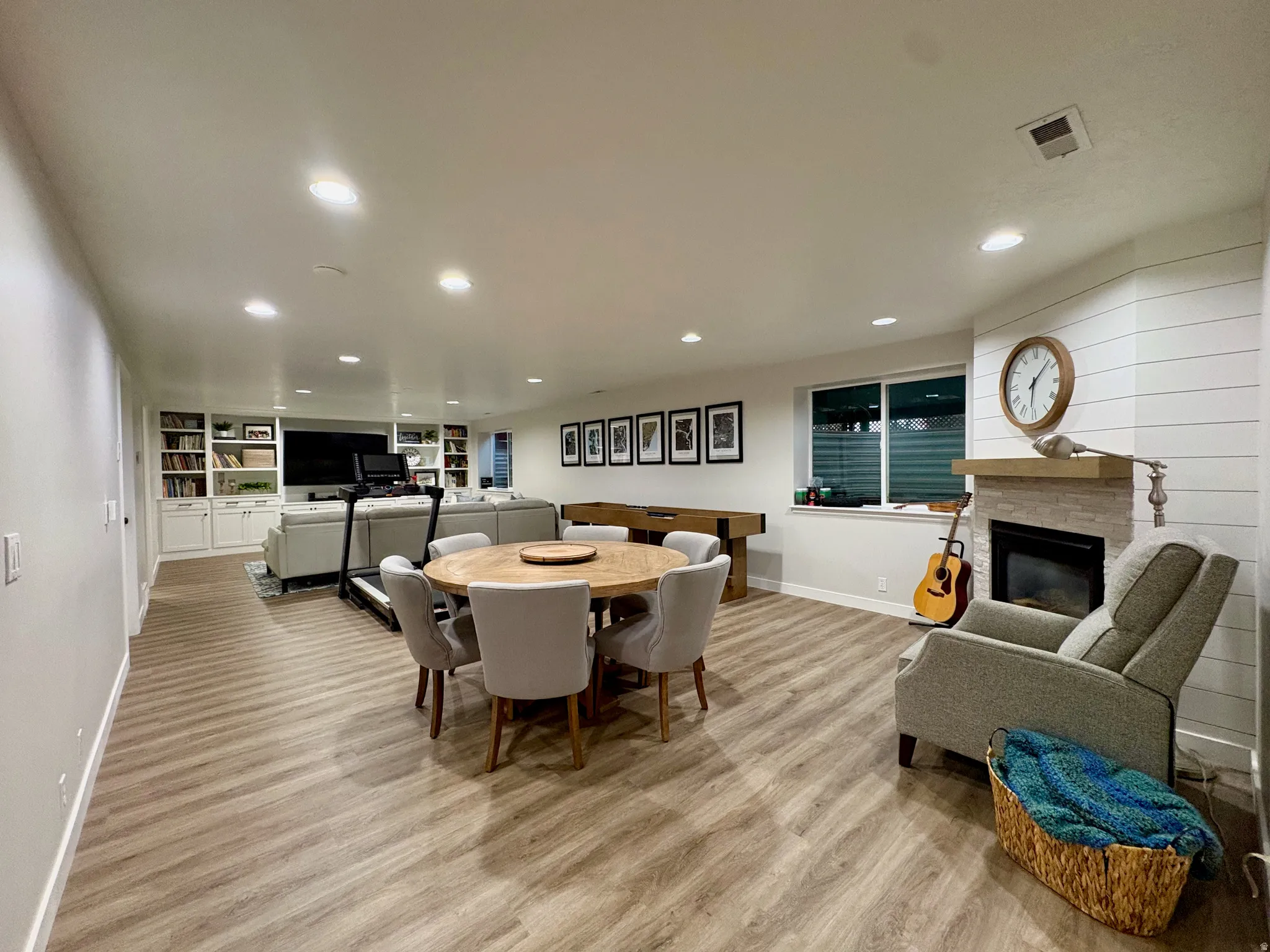Wood-finish flooring throughout, recessed lighting, built-in shelving, stone-surround fireplace with a wood mantel, and shiplap accent wall