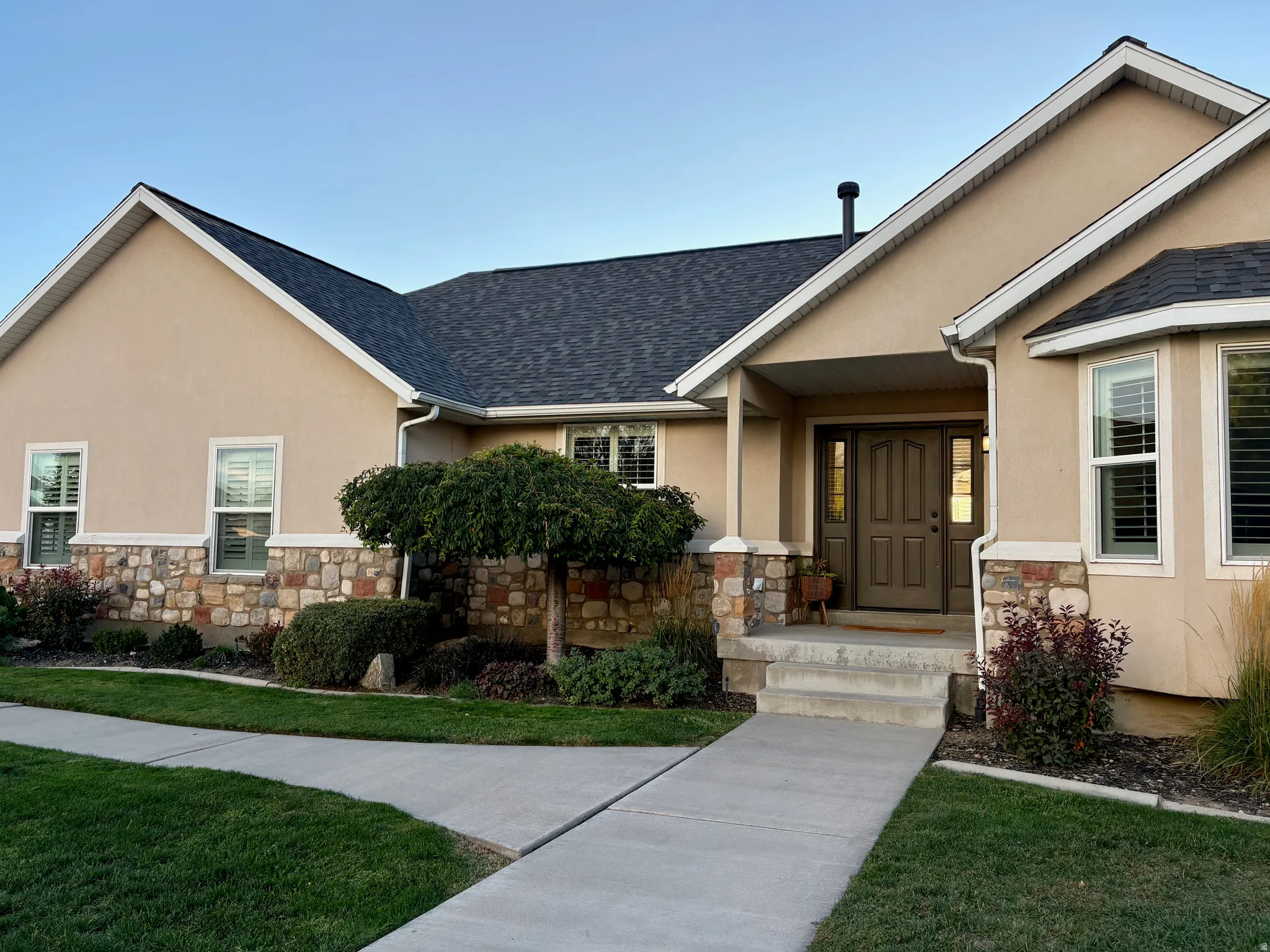Stucco exterior with stone veneer accents, dark shingle roofing, and a prominent covered entryway