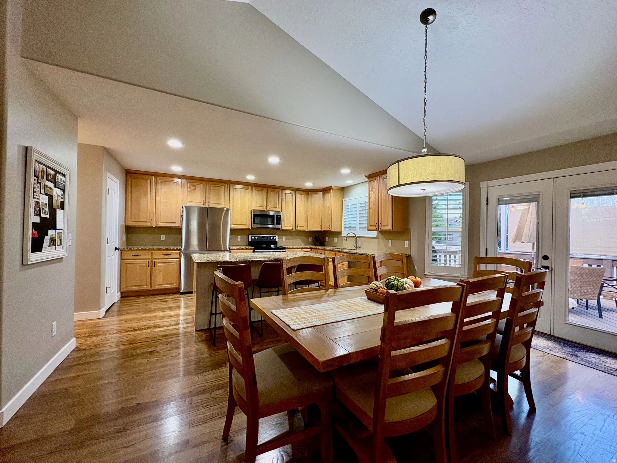 Kitchen and dining area featuring wood-finish flooring, light wood cabinetry, stainless steel appliances, a kitchen island, and French doors