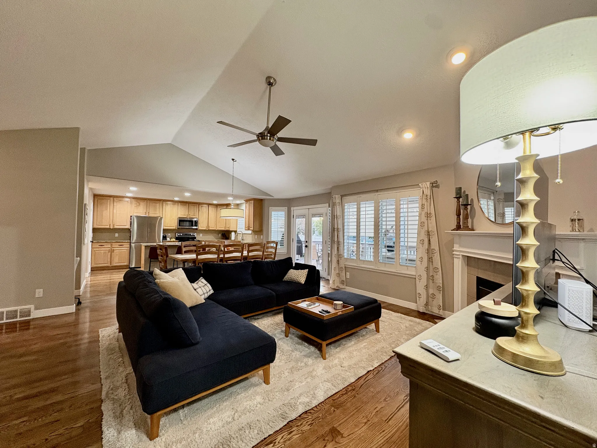 Vaulted ceiling, recessed lighting, wood-finish flooring, kitchen with light wood cabinetry, white plantation shutters