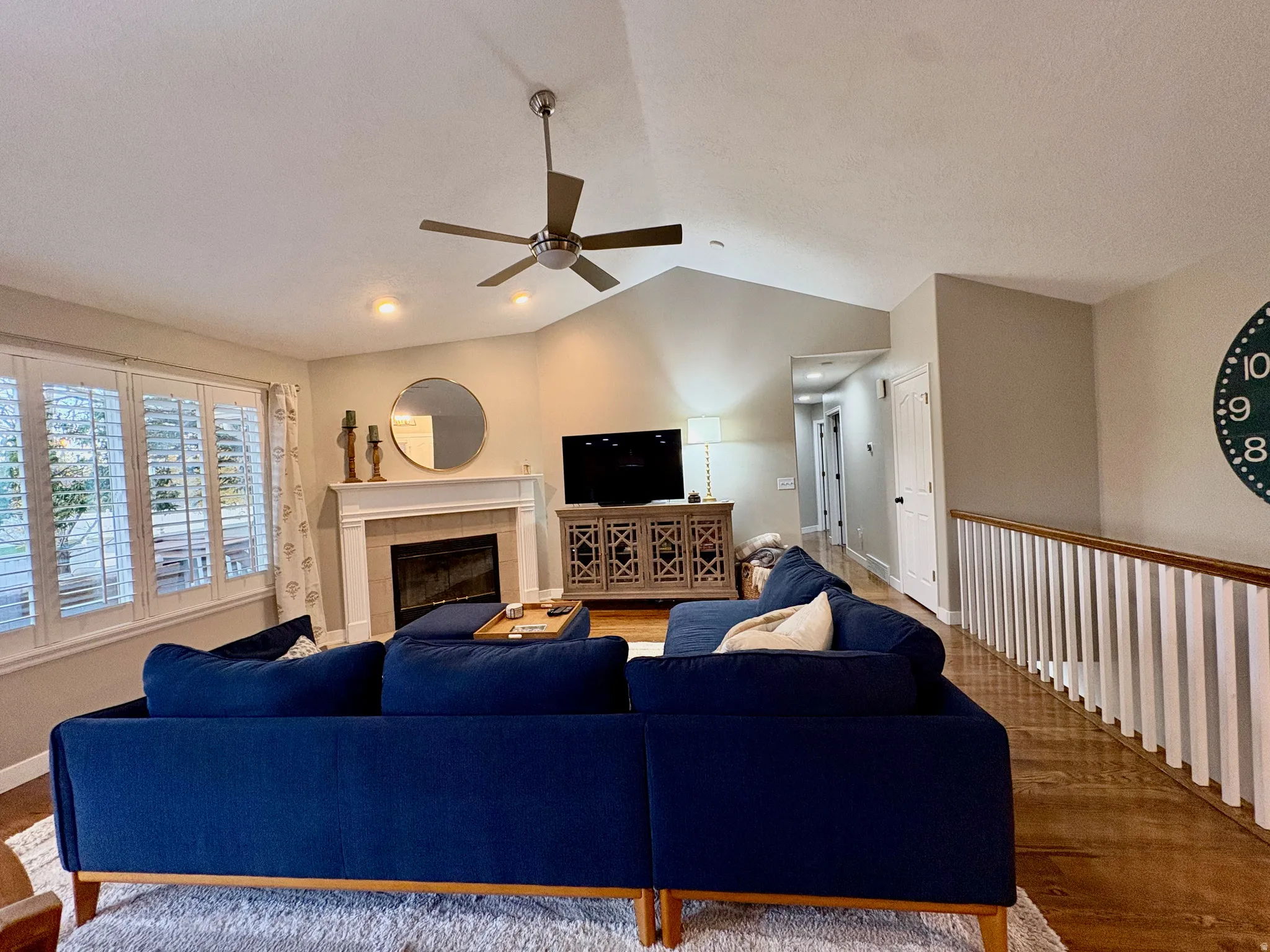 Vaulted ceiling with a ceiling fan, recessed lighting, fireplace with a mantel, and plantation shutters