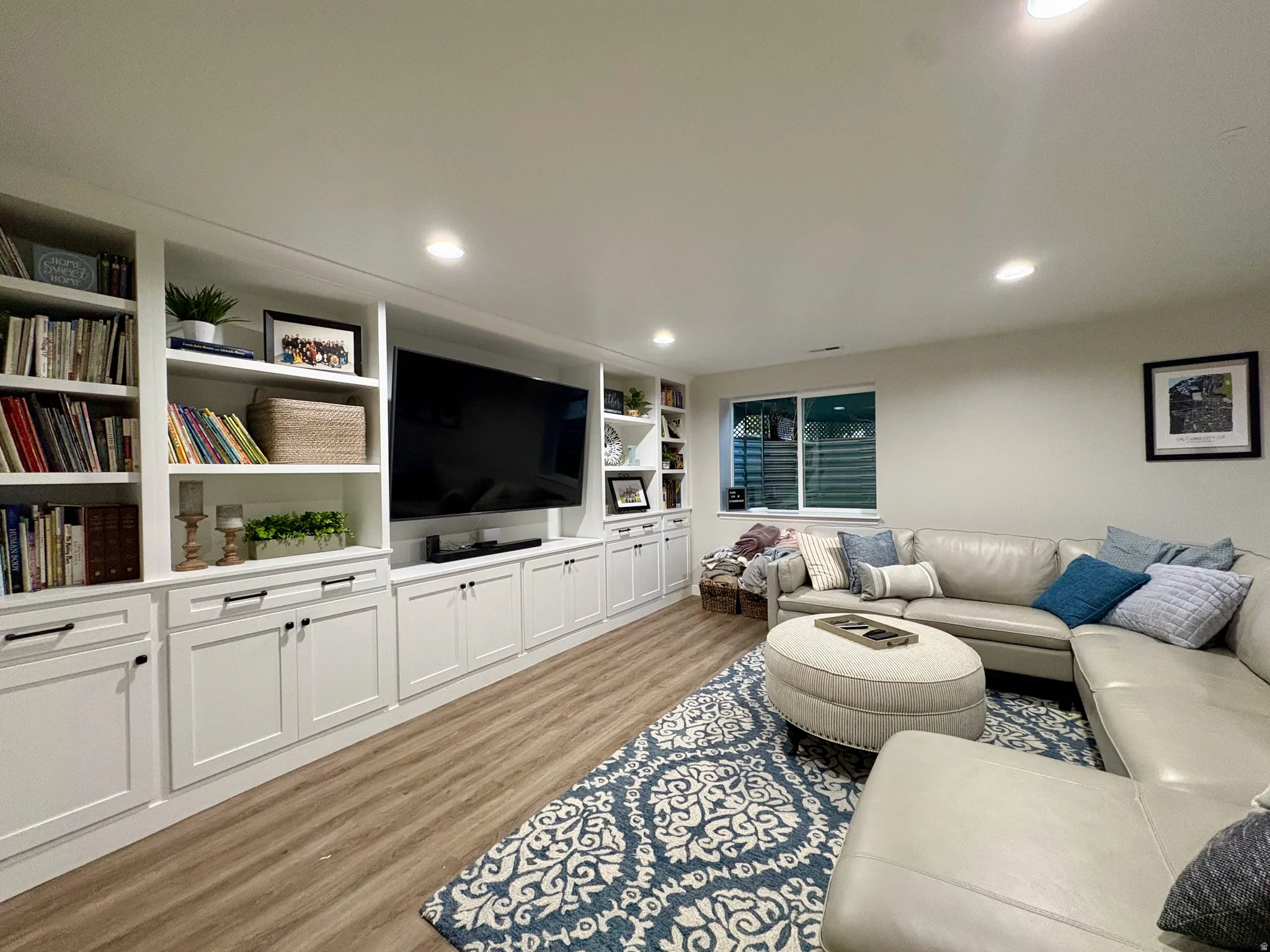 Custom built-in cabinetry with open shelving, recessed ceiling lighting, wood-finish flooring, and a white-framed window