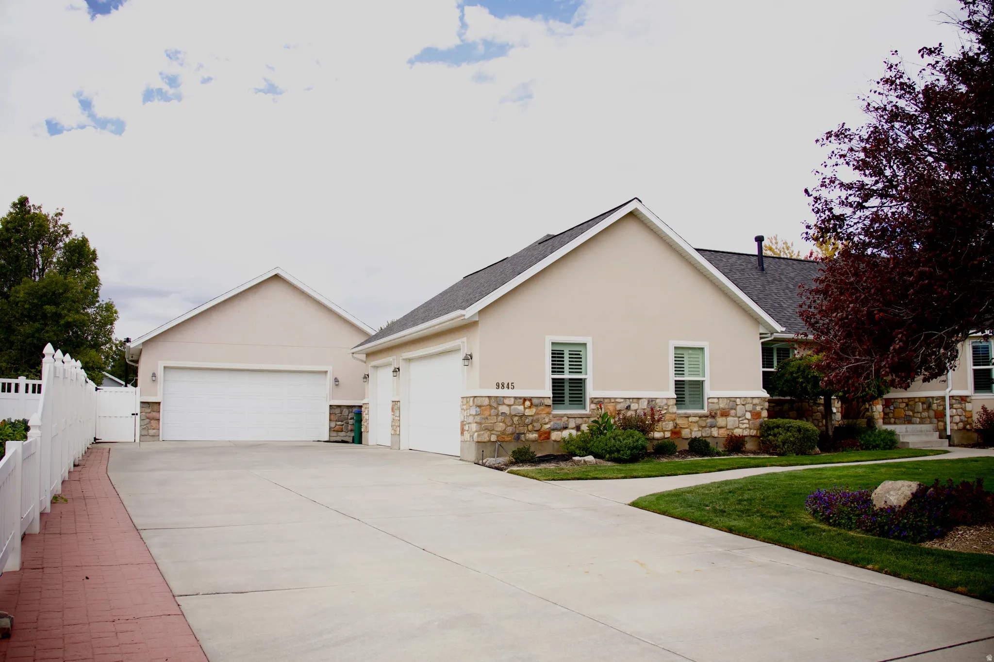 Exterior featuring a light stucco facade with stone accents, multiple garage bays, a paved driveway, and a white picket fence