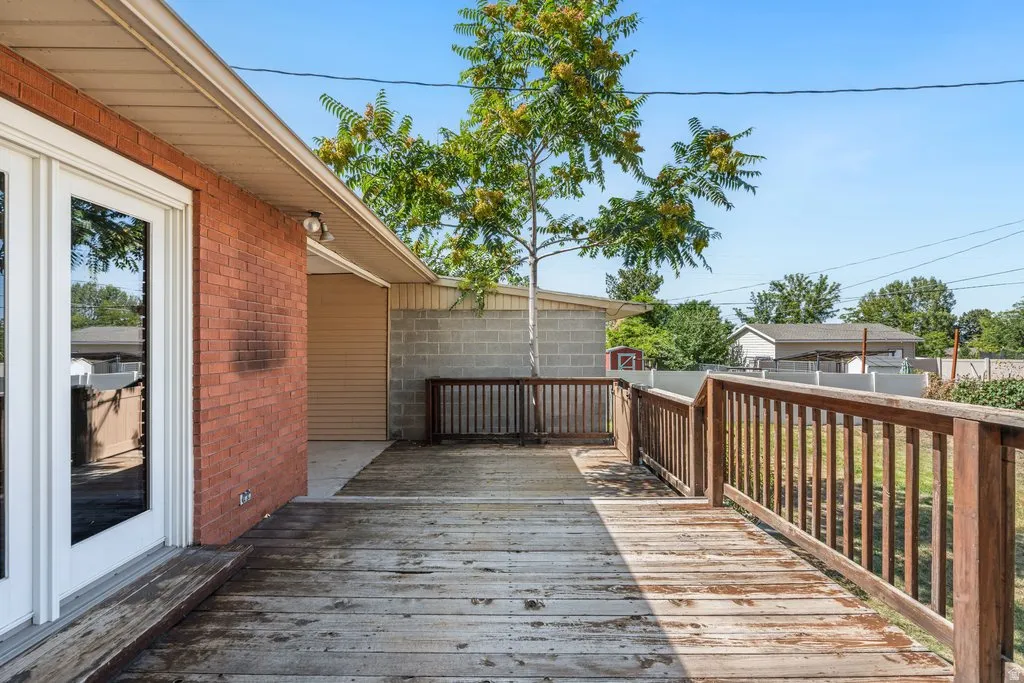 Wood deck with railing, brick exterior, double glass-paneled doors, and concrete block wall